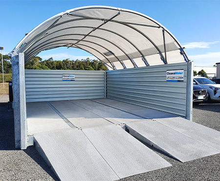 A real Cleanawater car wash bay with three walls and a roof, set up in a busy pa